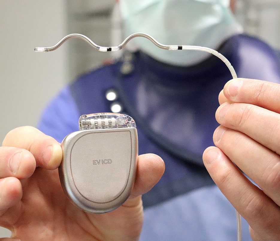 Zwei Hände halten einen Defibrillator und eine Elektrode in die Kamera.