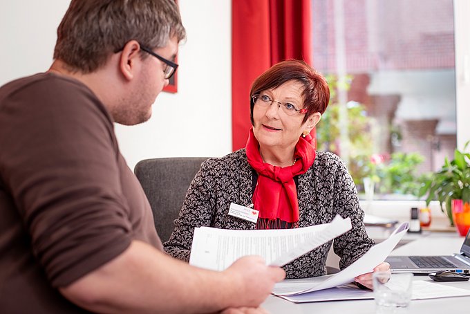 Dies zeigt eine Mitarbeiterin des Sozialdienstes im Gespräch mit einem Patienten.