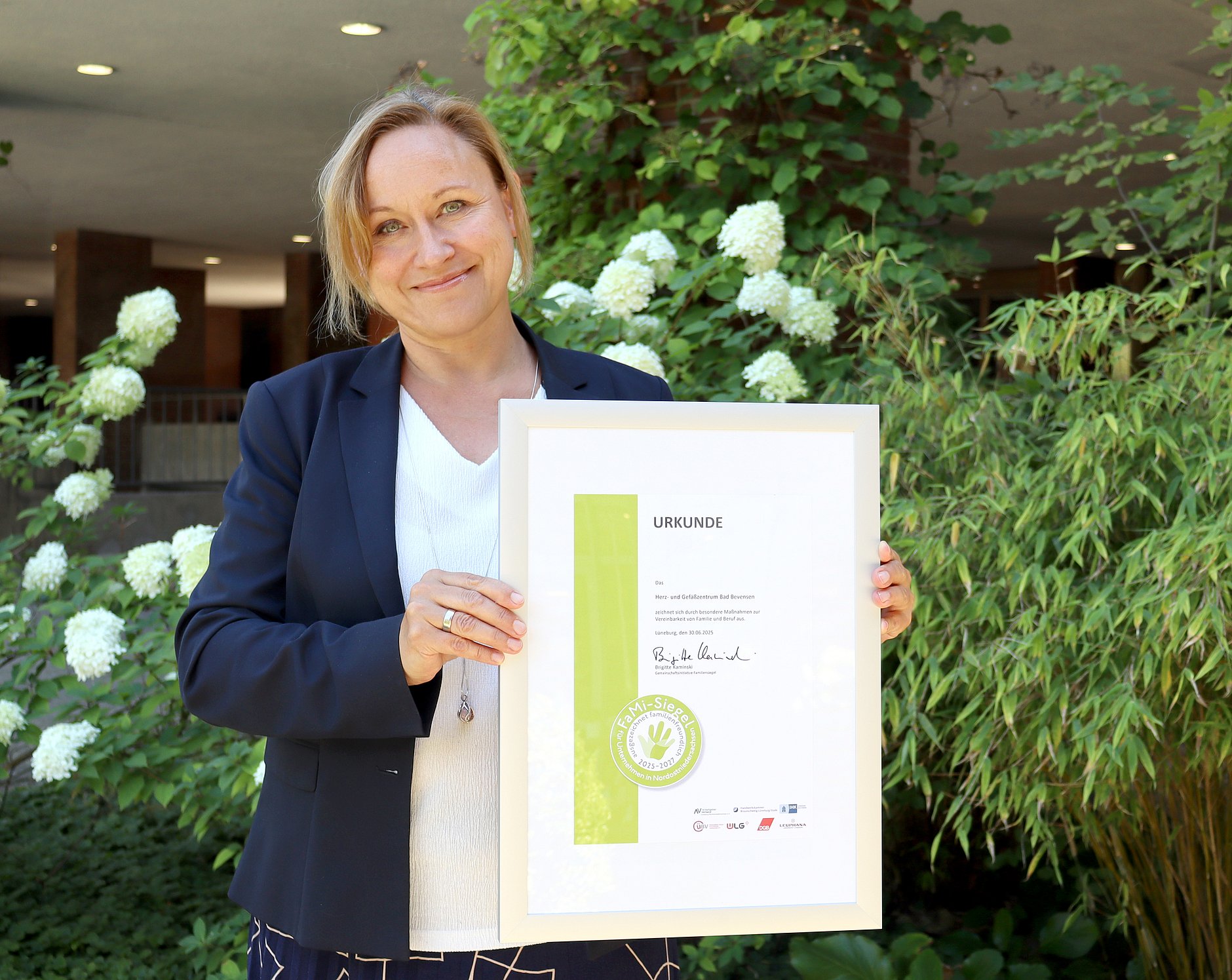 Die Personalleiterin präsentiert einen Bilderrahmen, in dem sich das Siegel für Familienfreundlichkeit befindet.