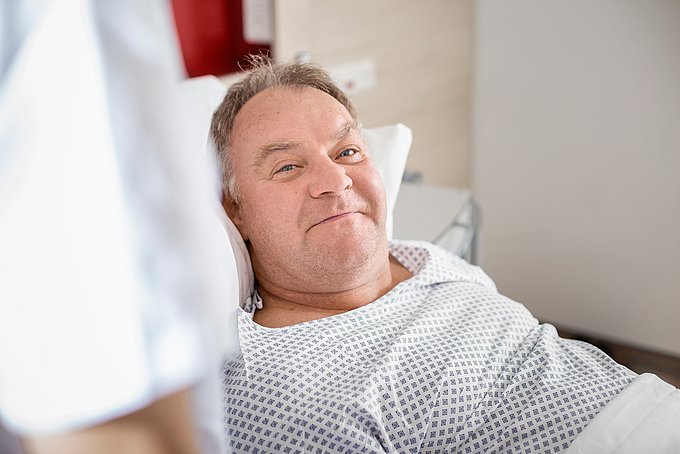 Dies zeigt einen lächelnden Patienten im Patientenbett.