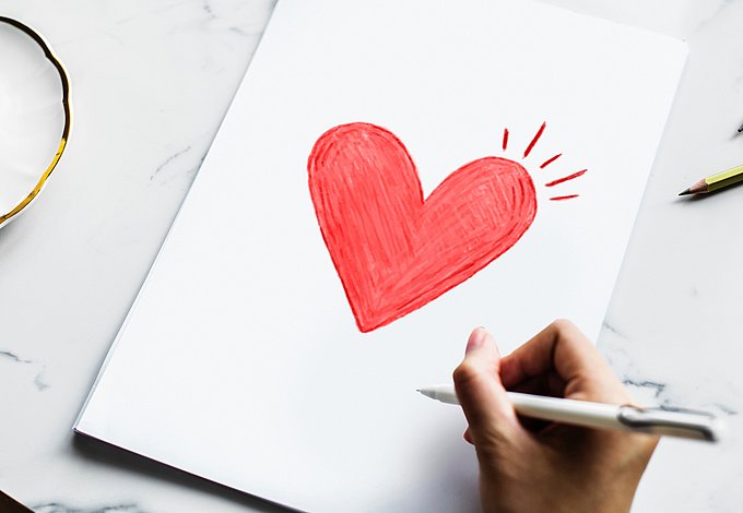 Dies ist ein gezeichnetes Herz, daneben eine Hand, die einen Stift hält.