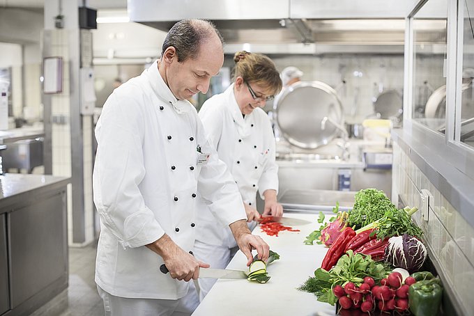 Dies zeigt zwei Köche beim Gemüse schneiden in der Küche des HGZ.